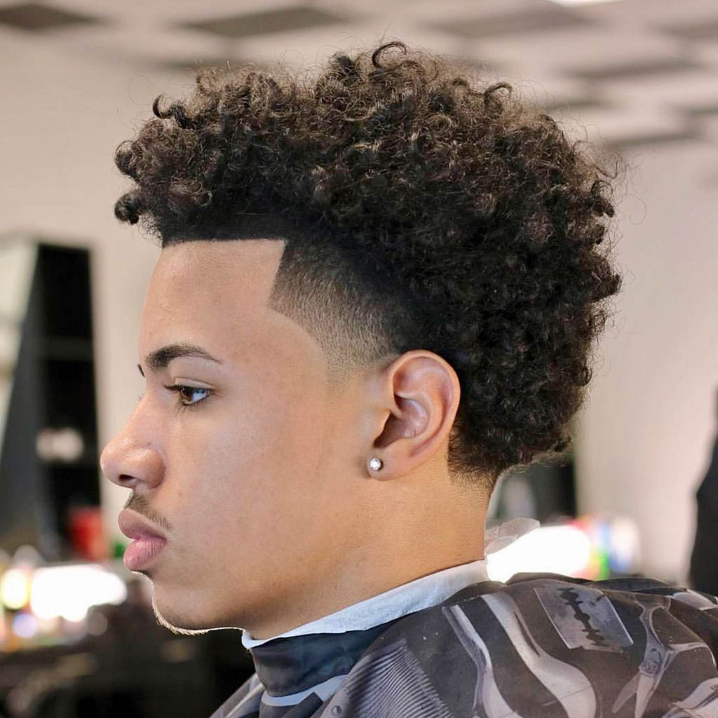 A man with a curly taper Natural Hairstyles for Men, featuring a gradual fade from shorter sides to longer, curly hair on top.